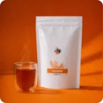 Dampfende Tasse Kalahari Rooibos Tee neben der Verpackung von MEE KAFFEE. Die praktischen Pyramidenbeutel ermöglichen den Rooibos-Blättern eine optimale Entfaltung und garantieren einen vollmundigen, milden und koffeinfreien Teegenuss.