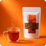 Kalahari Rooibos Tee von MEE KAFFEE mit frisch aufgebrühter Tasse Rooibos Tee auf orangefarbenem Hintergrund